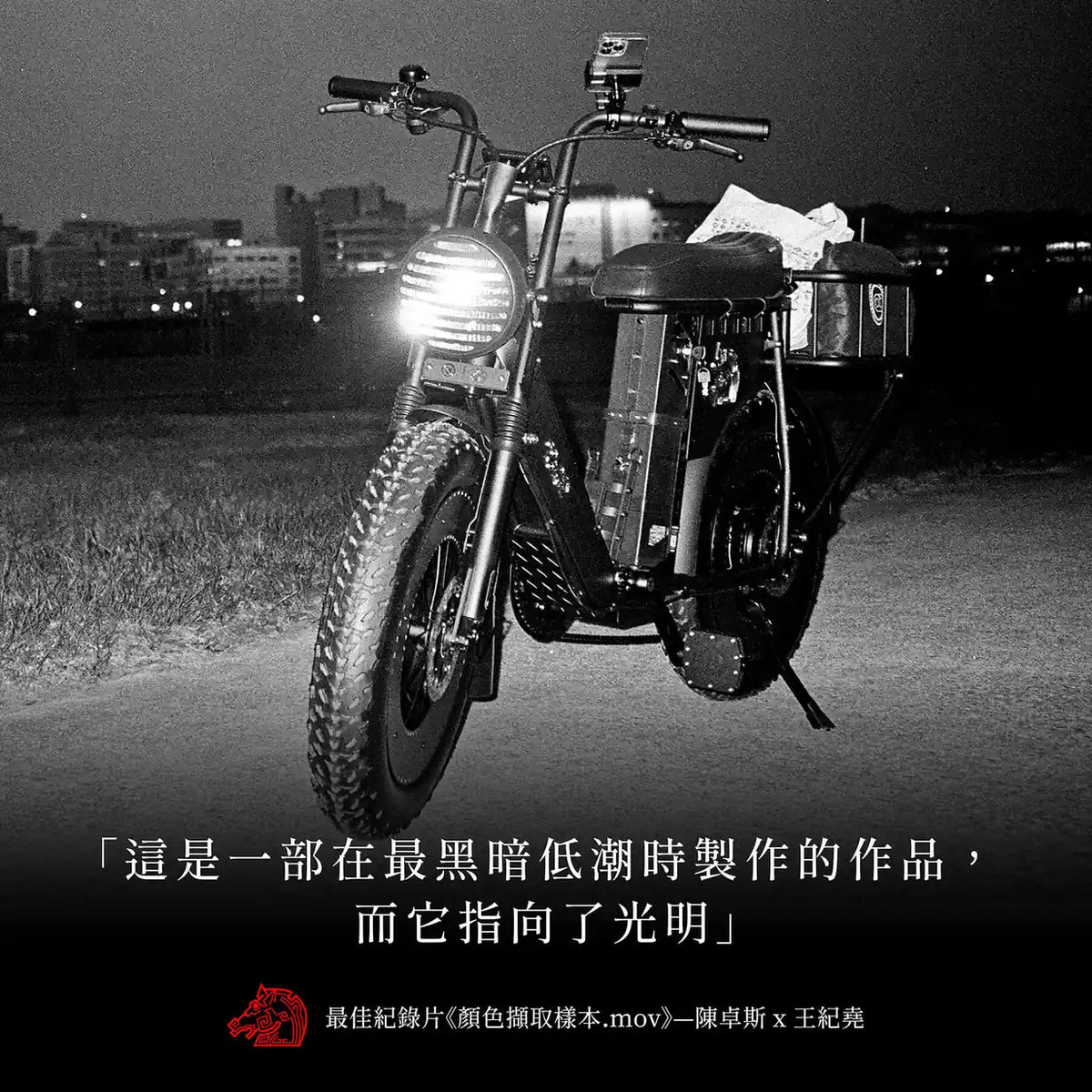 黑白夜景照片，一台胖胎電輔車停在河濱草地上亮著車頭燈，下方印著「這是一部在最黑暗低潮時製作的作品，而它指向了光明」
