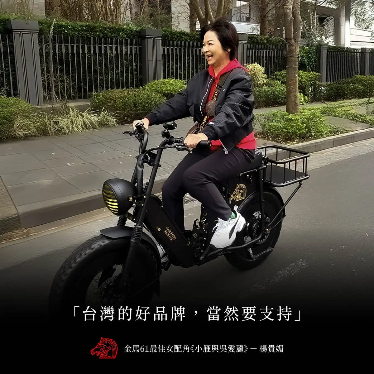 楊貴媚騎著黑色金馬號電輔車經過街道，笑著看向前方，下方印著「台灣的好品牌，當然要支持」