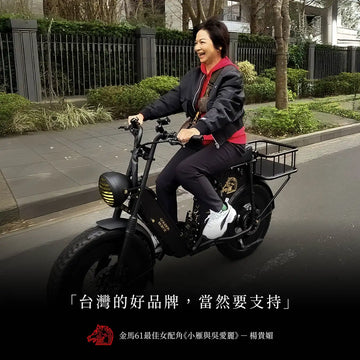 楊貴媚騎著黑色金馬號電輔車經過街道，笑著看向前方，下方印著「台灣的好品牌，當然要支持」