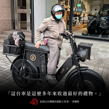李錫堅戴著安全帽跨坐在黑色胖胎電輔車上，停在門市櫥窗前，下方印著「這台車是這麼多年來收過最好的禮物。」