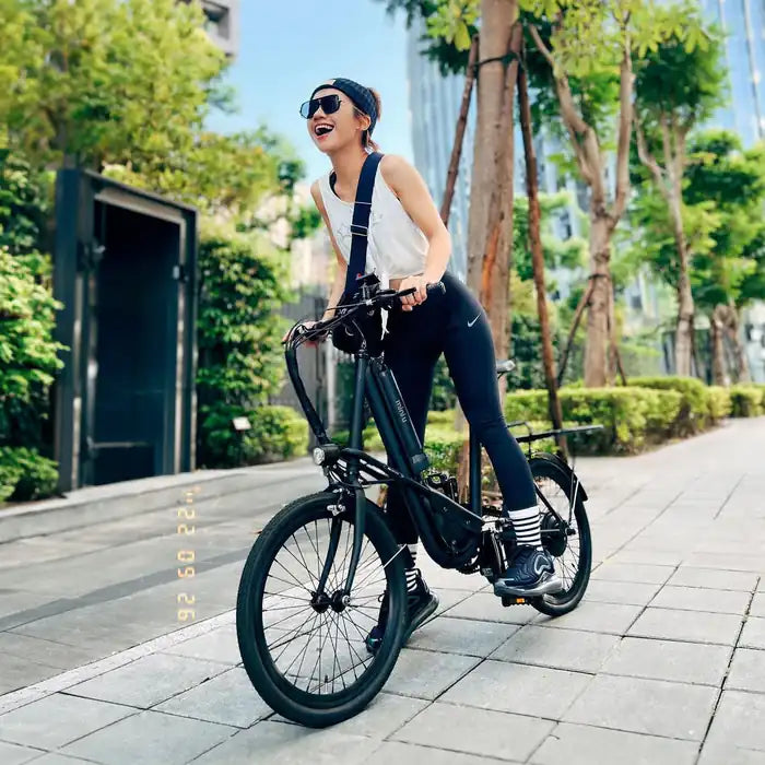 一位女生騎著黑色電輔車經過林蔭道