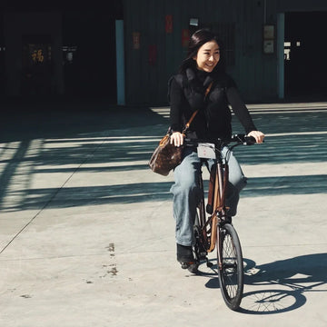 陽光下的廣場，女生騎著電輔車迎面而來，肩上背著一個包