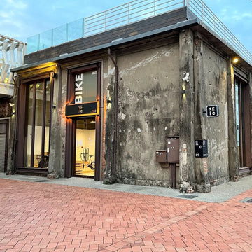 高雄駁二四號倉 SEic 單車工廠的店面外觀，灰色老倉庫外牆掛著 BIKE 招牌，前方是紅磚廣場