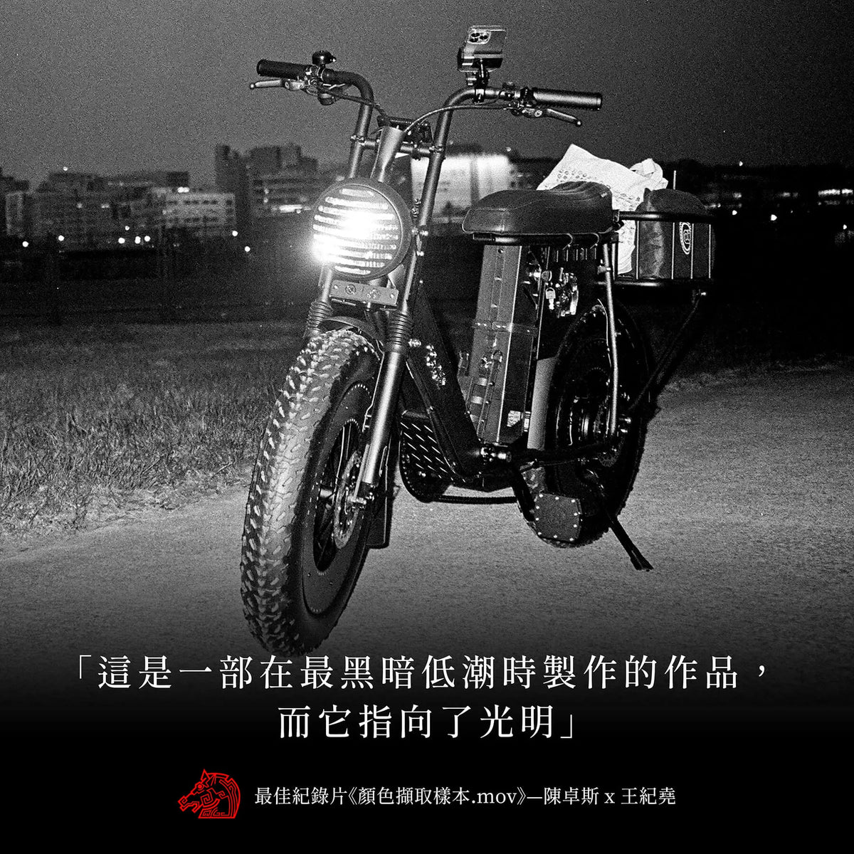 黑白夜景照片，一台胖胎電輔車停在河濱草地上亮著車頭燈，下方印著「這是一部在最黑暗低潮時製作的作品，而它指向了光明」