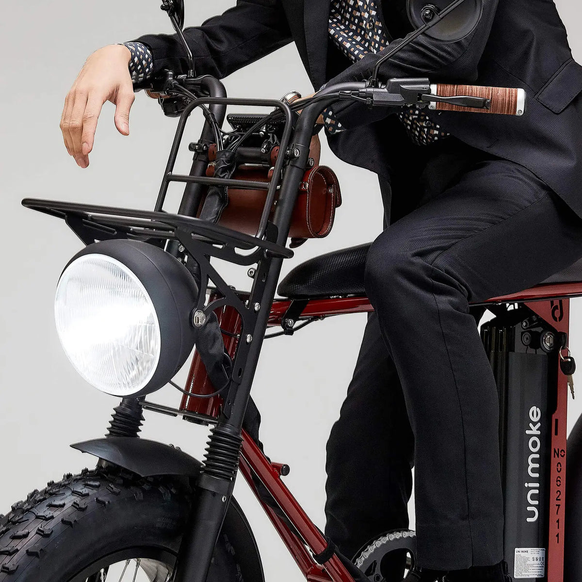 身穿黑色西裝的人騎乘酒紅色 Unimoke 電動單車，配有大燈、前置置物架和胖胎，手握皮質車把握把