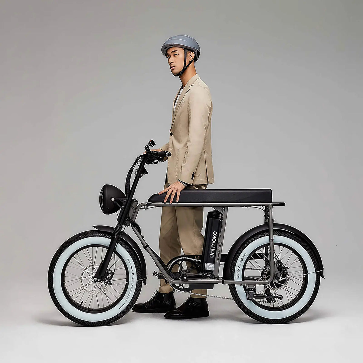 一個戴著西班牙安全帽的男人牽著 Unimoke MK 銀色，風格時尚復古