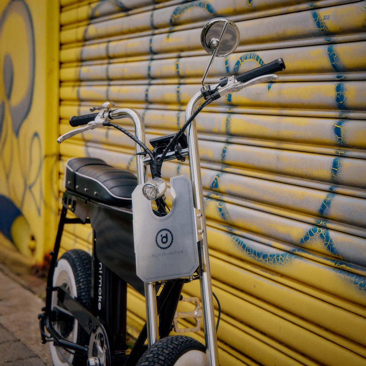 minibike 珍珠黑停在有噴漆的鐵捲門前，加裝賽車板風格強烈，同時具復古和街頭風格