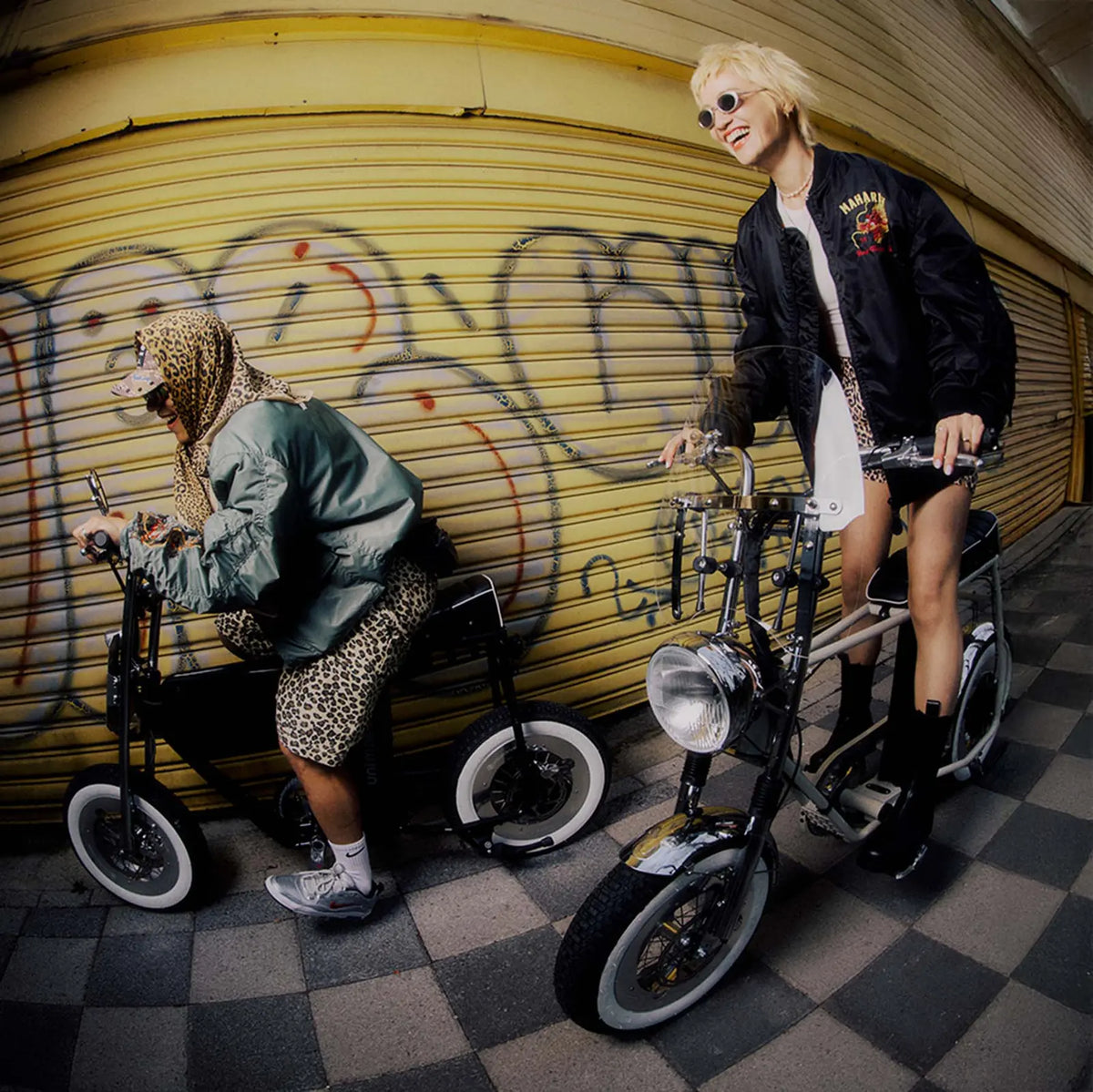 一對男女在鐵捲門前騎著 minibike ，展示街頭風格